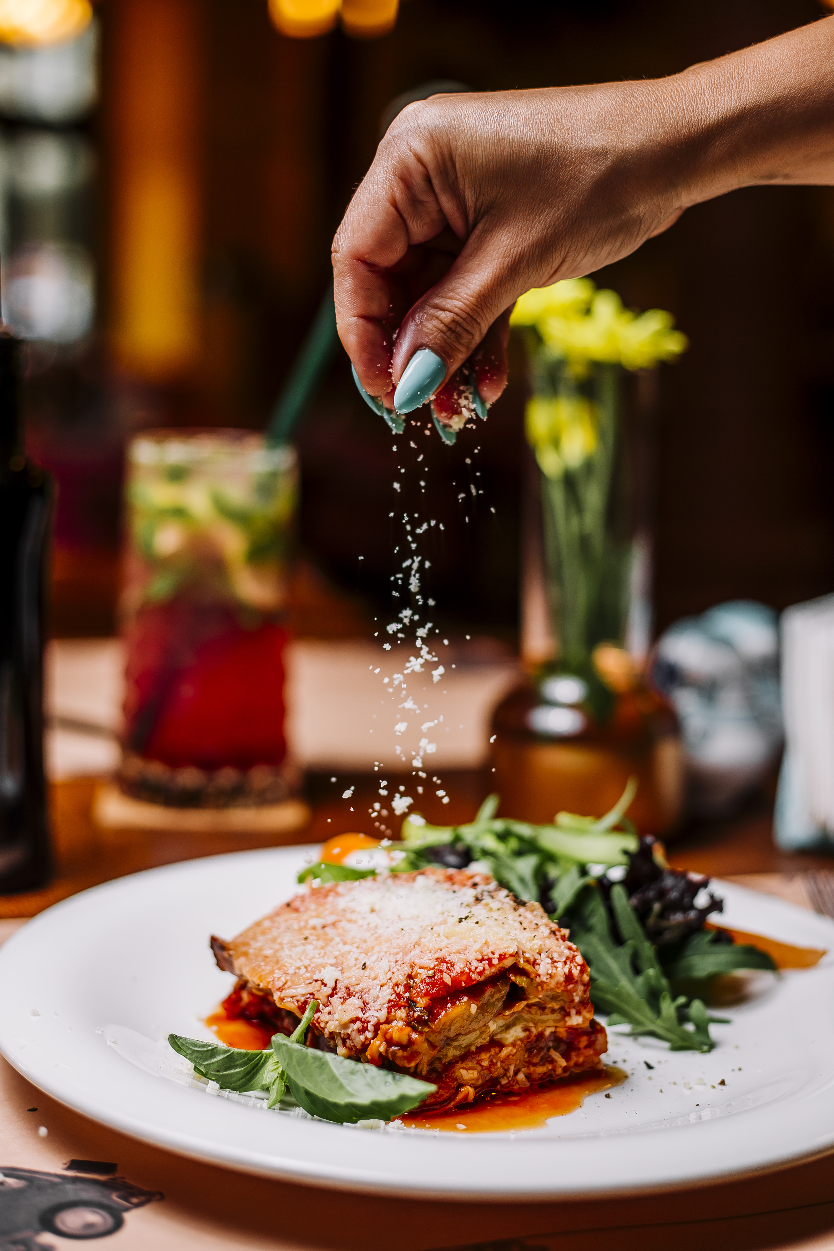 woman sprinkles grated parmesan particles on lasagne